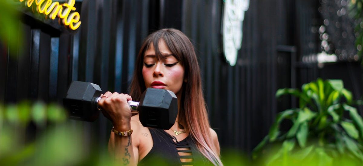 Fitness woman with long hair lifting a dumbbell outdoors, focusing on her strength training.