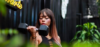 Fitness woman with long hair lifting a dumbbell outdoors, focusing on her strength training.