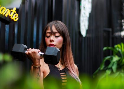 Fitness woman with long hair lifting a dumbbell outdoors, focusing on her strength training.