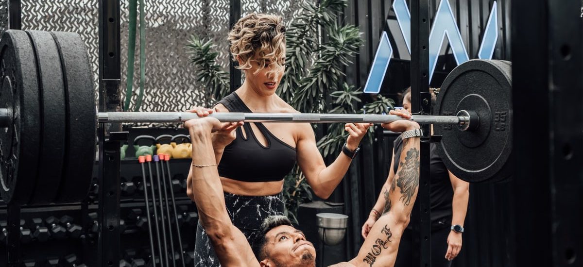 Man lifting weights with woman spotting in Mexico City gym. Urban and dynamic fitness scene.