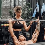Man lifting weights with woman spotting in Mexico City gym. Urban and dynamic fitness scene.
